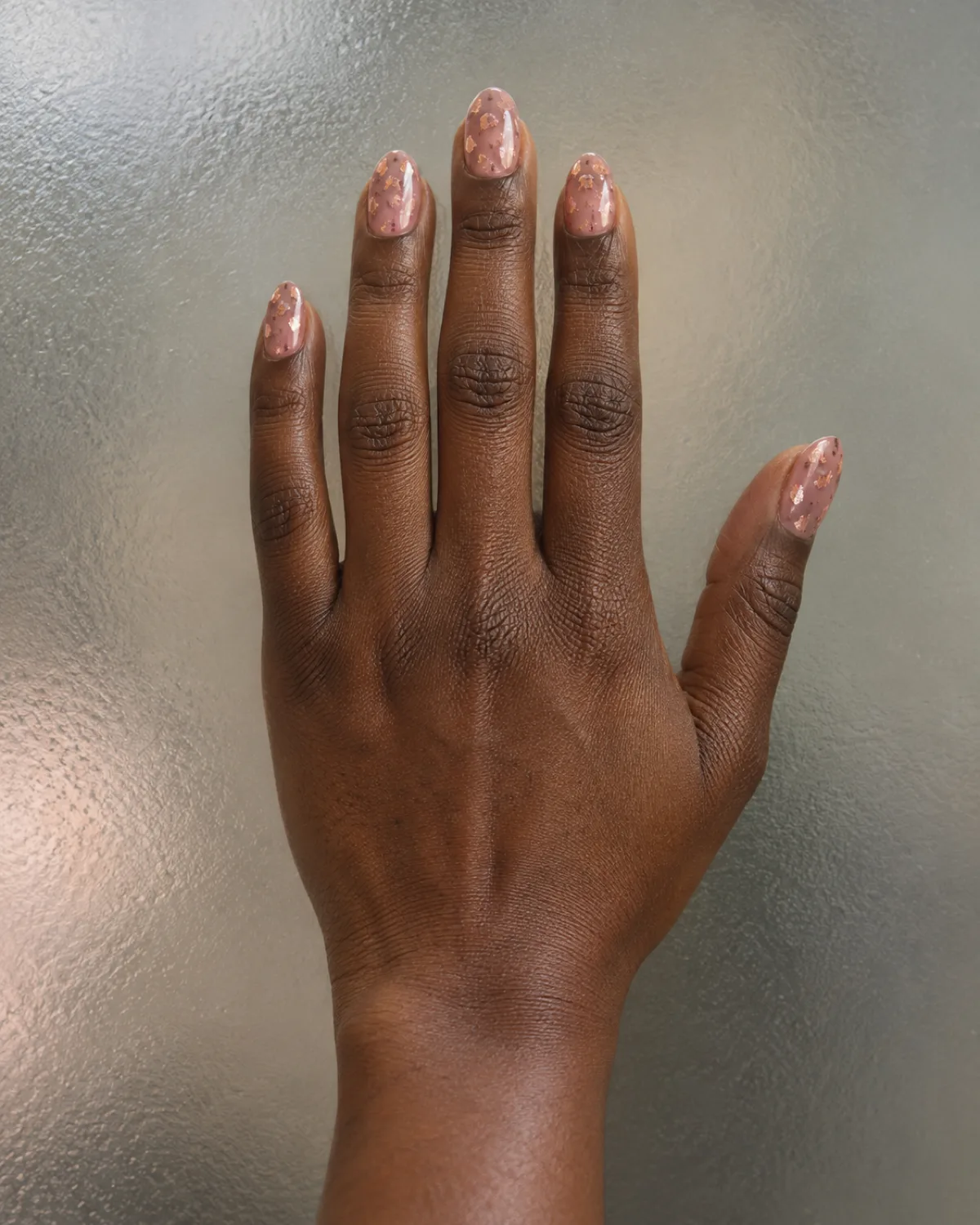 Single right hand with oval nails showing translucent jelly pink base with rose gold flakes on frosted glass surface