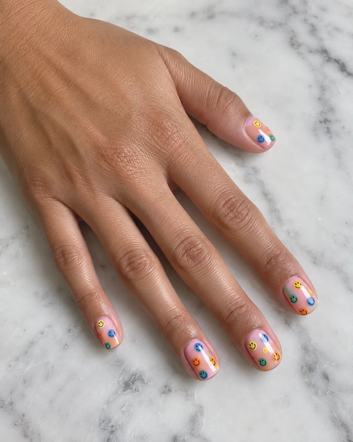 Single left hand with micro smiley scatter nails on short squoval shape resting on a smooth white marble board