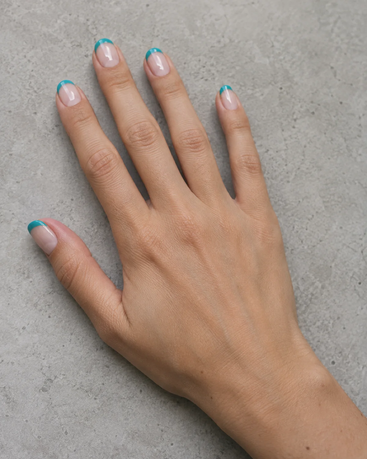 Single right hand with light teal French tips on sheer nude base resting palm down on light grey concrete countertop
