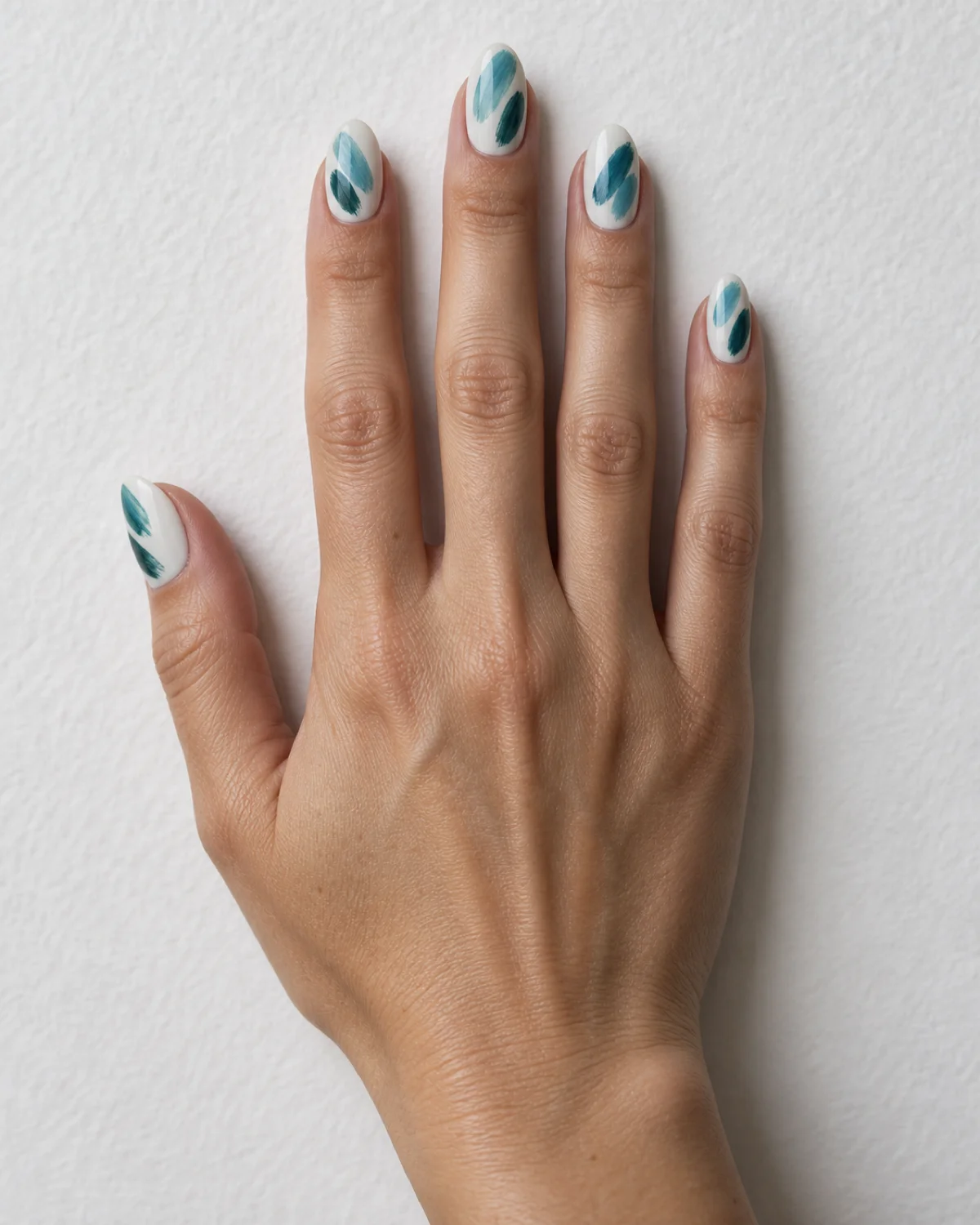 Single right hand with oval nails showing teal brushstrokes on white base resting palm down on white watercolor paper