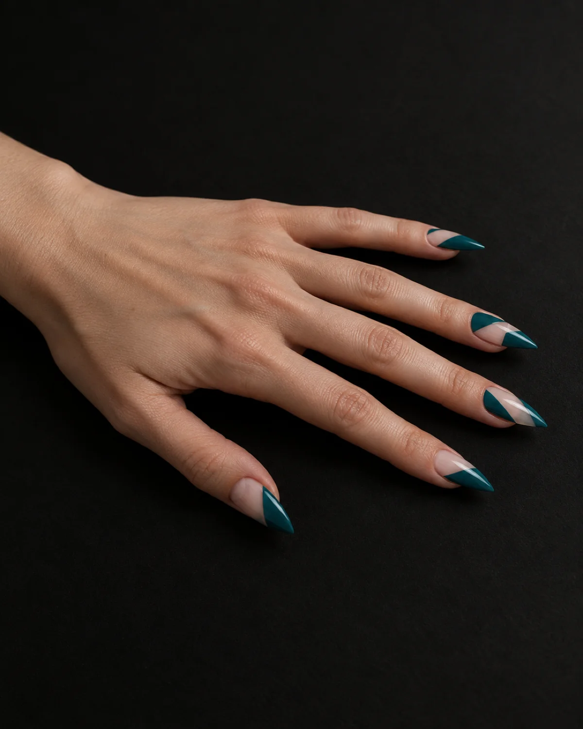 Single left hand with stiletto nails showing teal geometric blocks with negative space on clear base resting palm down on matte black surface