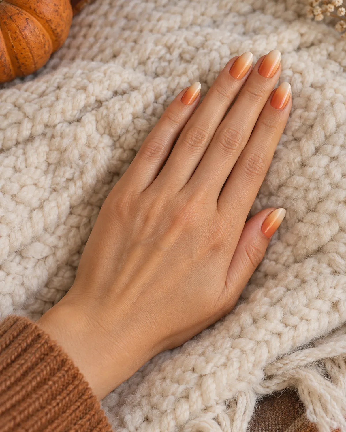 Pumpkin spice ombre nails on oval shape fading from warm orange at cuticle to soft cream at tip on cream wool blanket