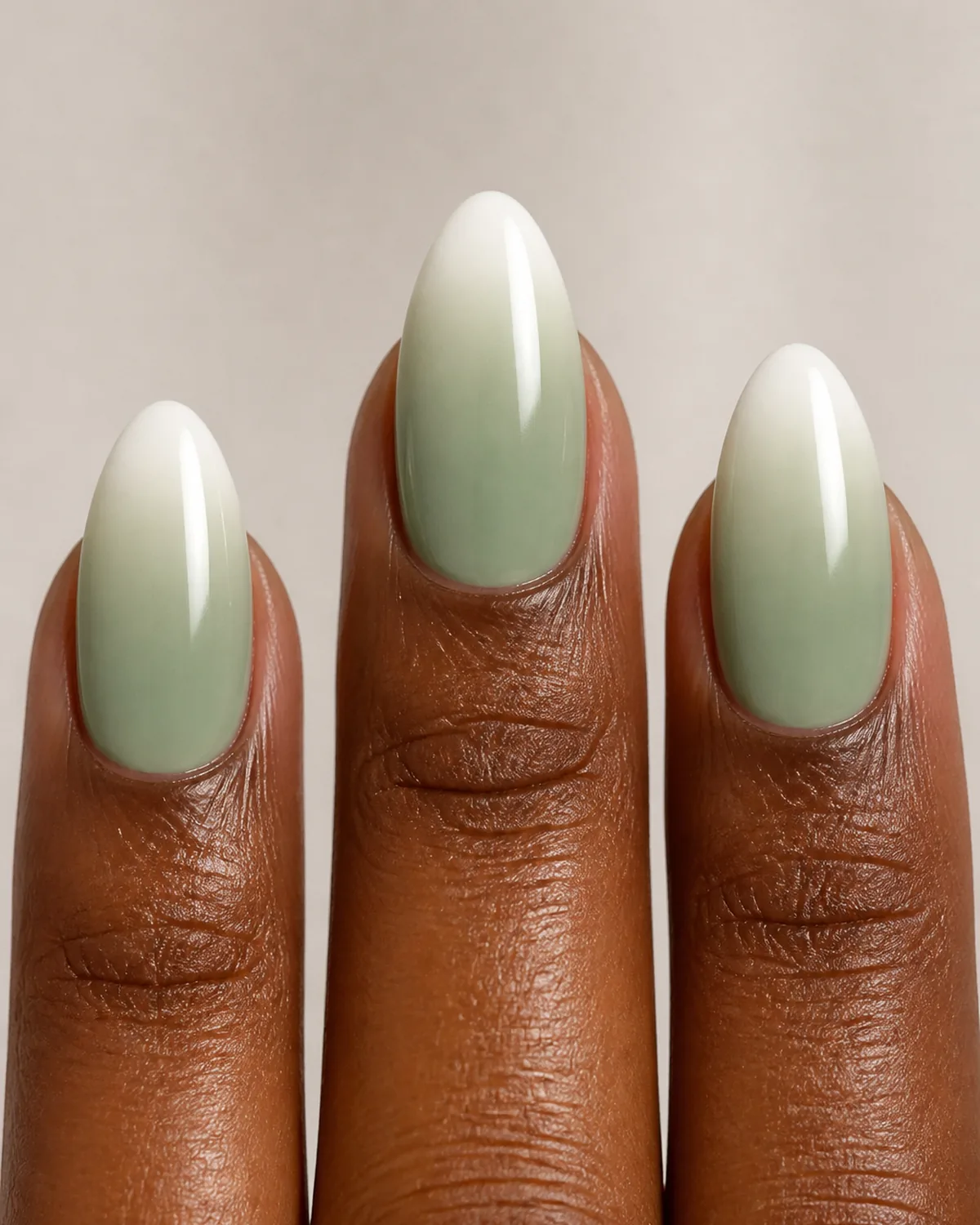Extreme close-up macro of three fingertips with medium almond nails featuring ombre French with sage green base fading to white tips