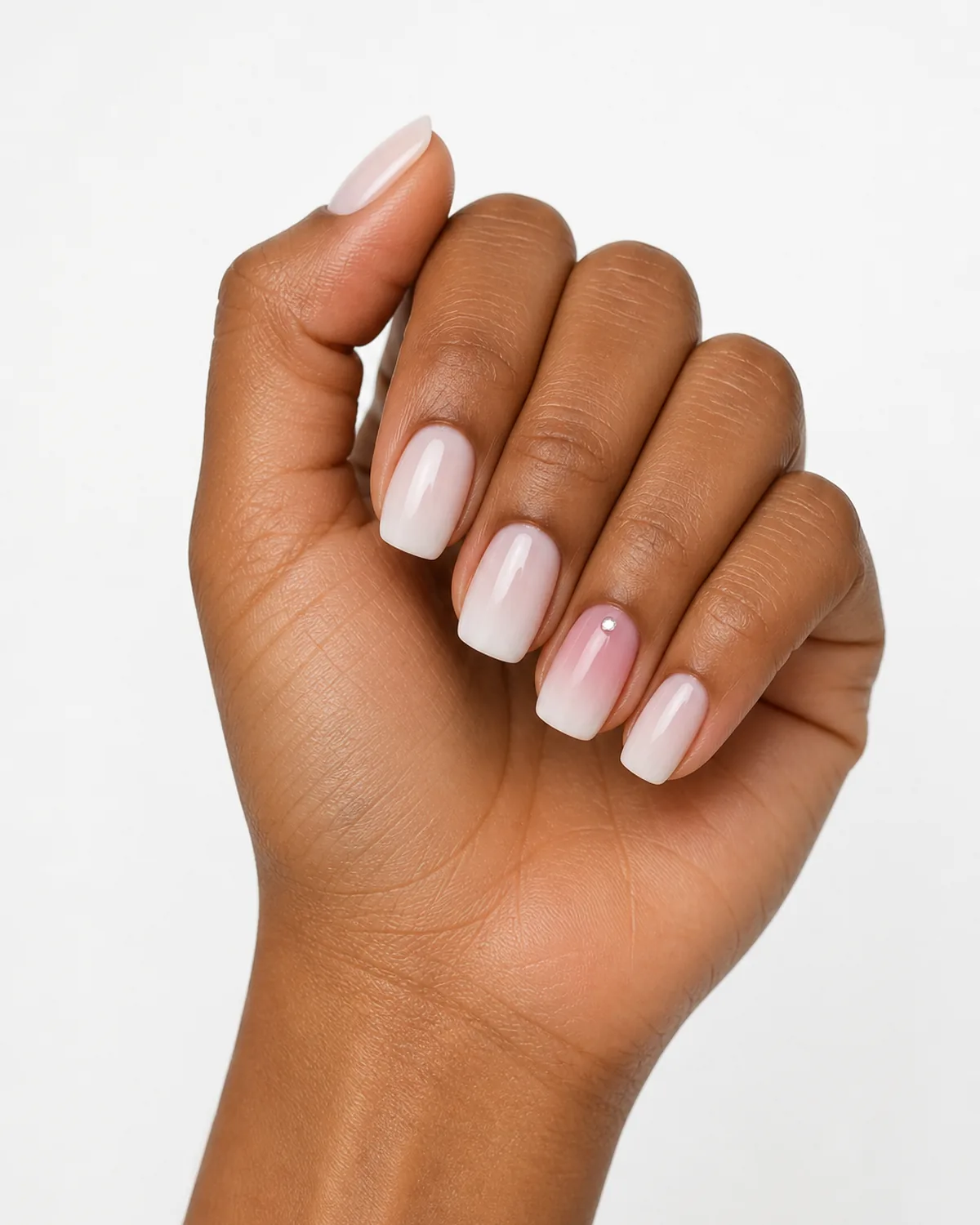 Single left hand in loose relaxed curl with nails facing camera medium squoval nails featuring milky ombre with accent ring finger crystal