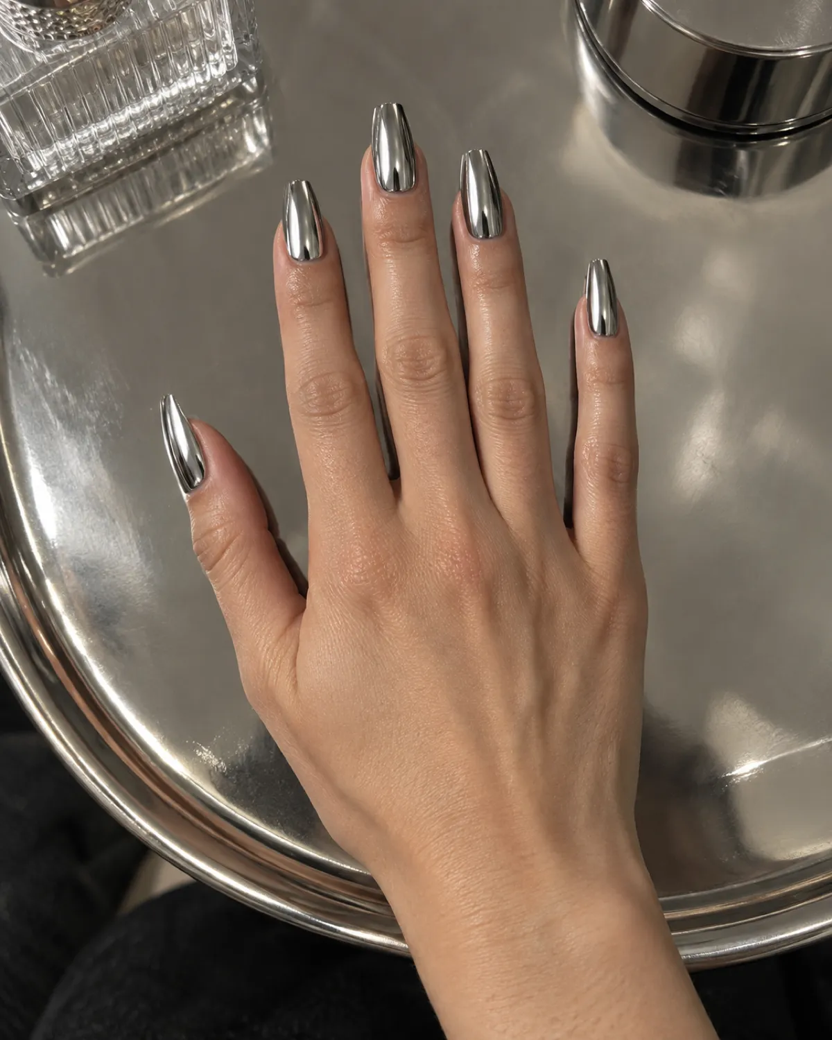 Single right hand with coffin nails in mirror chrome silver finish palm-down on reflective chrome tray surface
