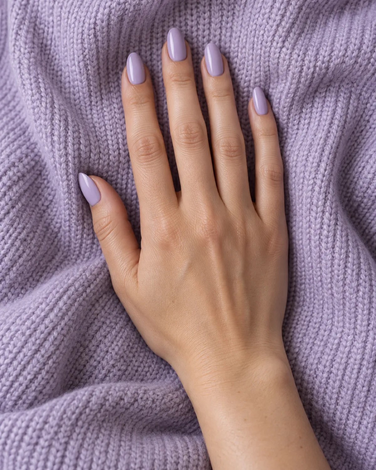 Single right hand with almond nails in opaque soft lilac crème polish palm-down on a lavender knit sweater