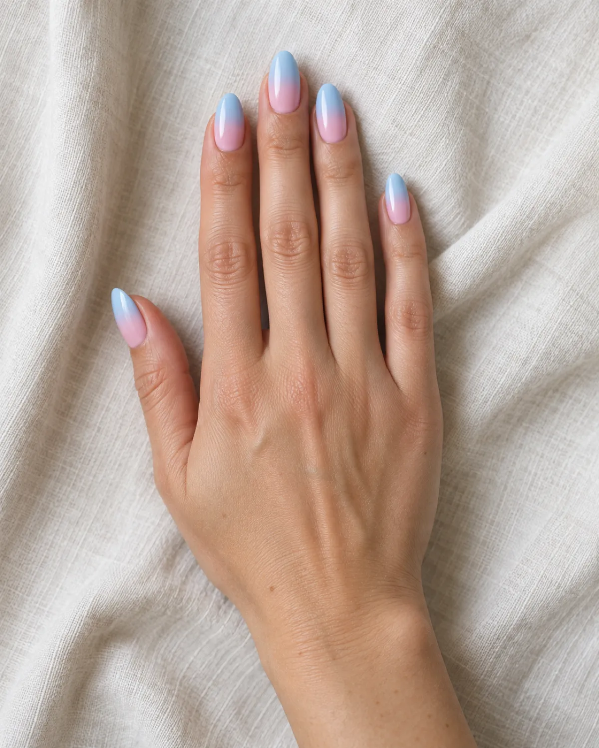 Single right hand with almond nails in cotton candy pink-to-blue gradient palm-down on cream linen cloth