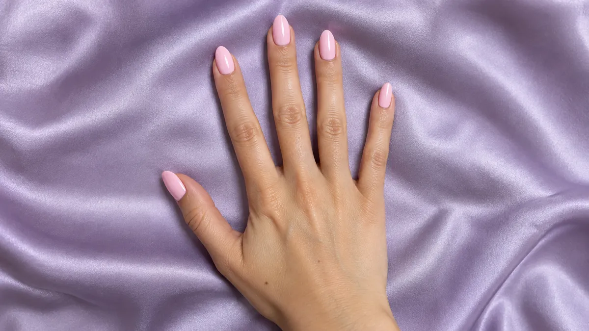 Single right hand with almond nails in opaque baby pink glossy crème polish splayed flat palm down on lilac satin surface